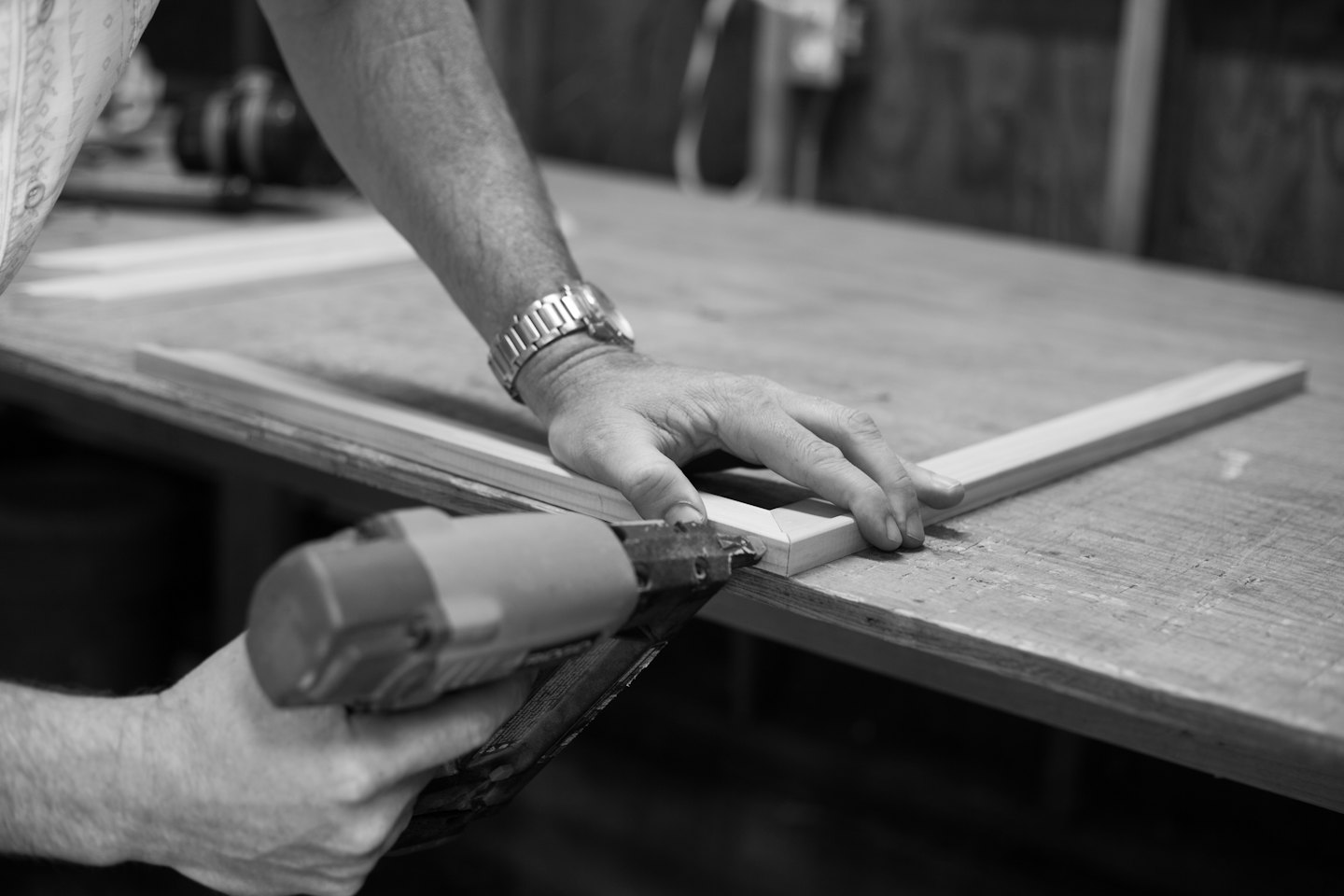 Hands assembling a wooden picture frame with a nail gun.