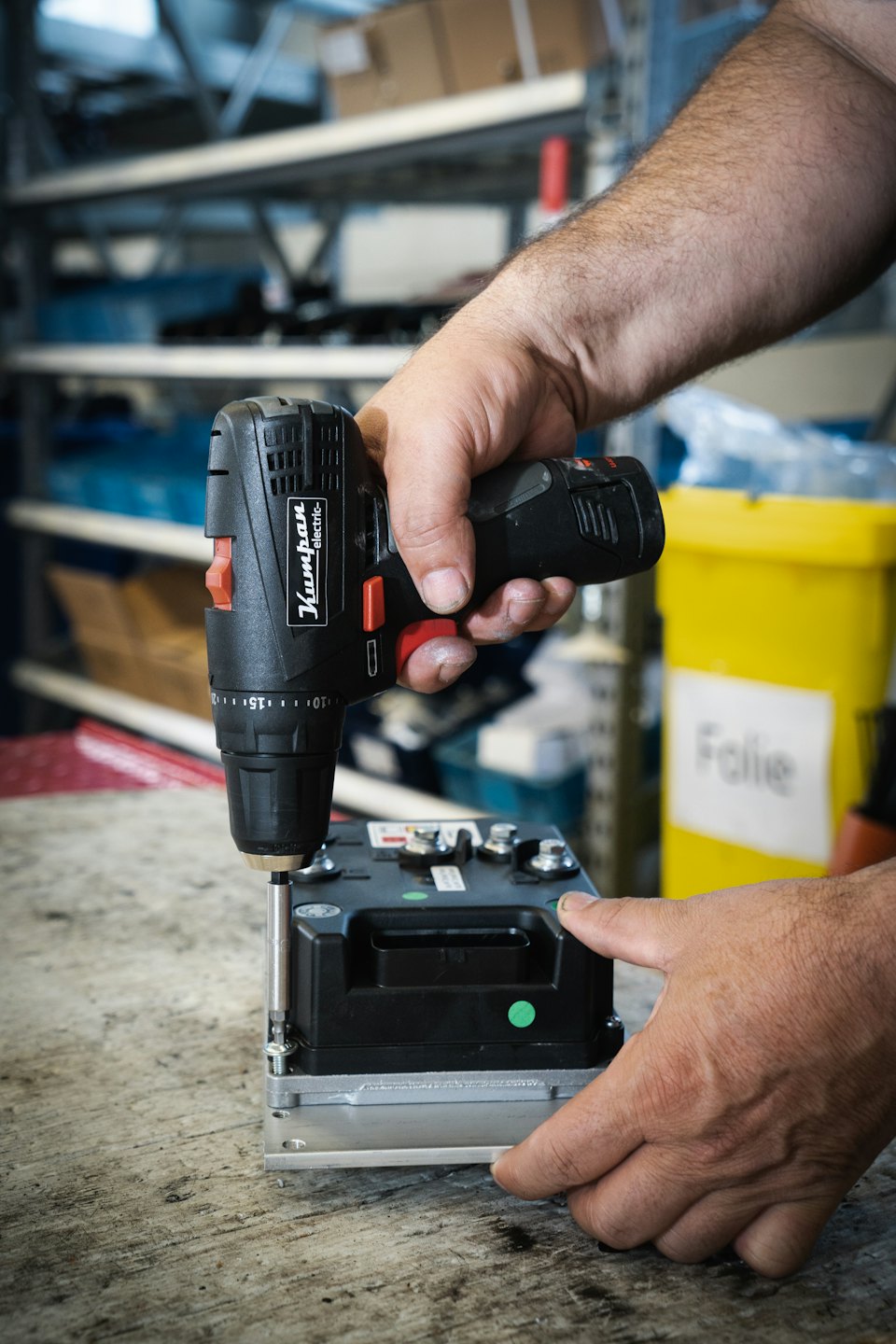 Hands using a black power drill on a wooden workbench.